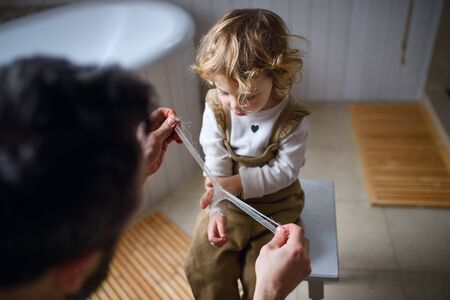 Father putting bandage on small hurt toddler child indoors at home.の写真素材