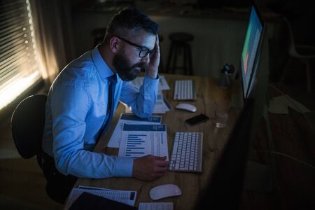 Frustrated businessman with computer sitting at desk, working late. Financial crisis concept.の写真素材