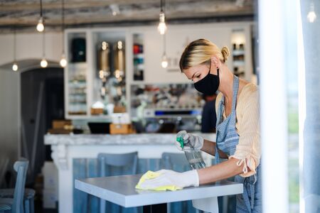 Coffee shop woman owner working with face mask and gloves, disinfecting tables.の写真素材