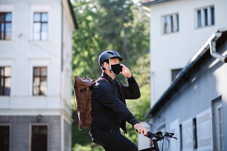 Delivery man courier on bicycle with face mask and smartphone delivering in town.の写真素材