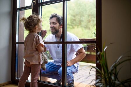 Doctor coming to see family in isolation, window glass separating them.の写真素材