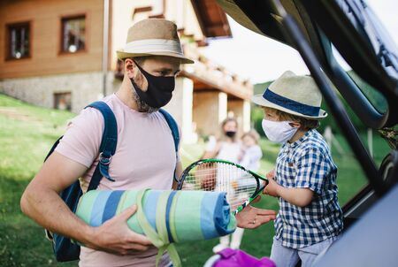 Family with two small children loading car for trip in countryside, wearing face masks.の写真素材