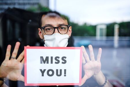 Portrait of sad man with face mask holding miss you sign, quarantine and lockdown concept.の写真素材