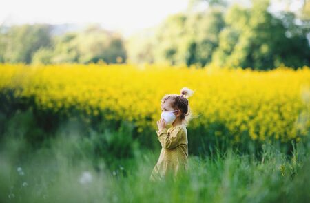 Side view of small toddler girl with face mask standing in nature in rapeseed field.の写真素材