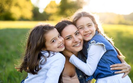 Mother with two small daughters having fun outdoors in spring nature, hugging.の写真素材