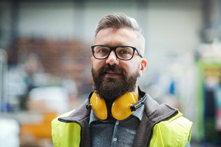 Technician or engineer with protective headphones standing in industrial factory.