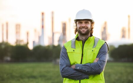 Young engineer standing outdoors by oil refinery, looking at camera.の写真素材