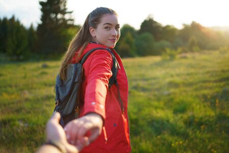 Young woman with backpack in summer nature, looking over shoulder at man.の写真素材