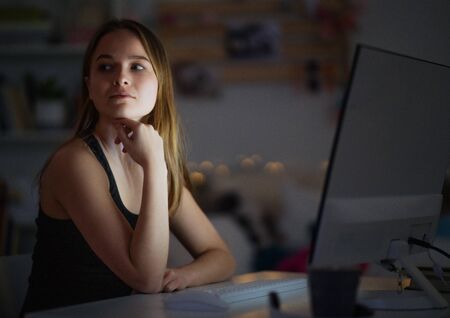 Young girl with computer sitting at desk at night, online dating concept.の写真素材