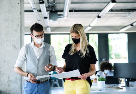 Young people with face masks back at work in office after lockdown.