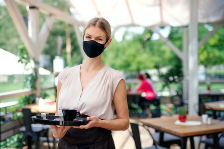 Waitress with face mask serving customers outdoors on terrace restaurant.の写真素材