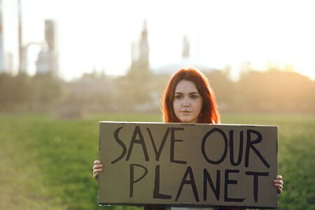 Young woman activist with placard standing outdoors by oil refinery, protesting.の写真素材