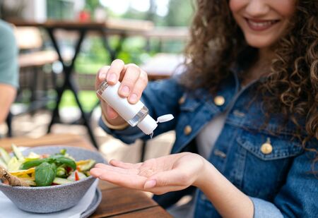 Unrecognizable woman sitting outdoors on terrace restaurant, disinfecting hands.の写真素材