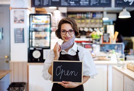 Young woman with face mask working in cafe, holding open sign.の写真素材