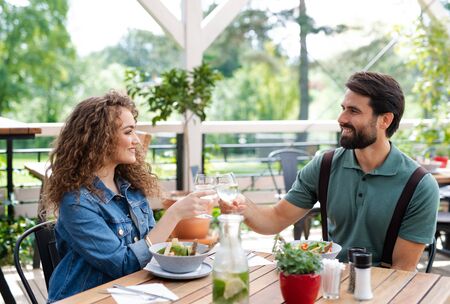 Happy couple sitting outdoors on terrace restaurant, clinking glasses.の写真素材