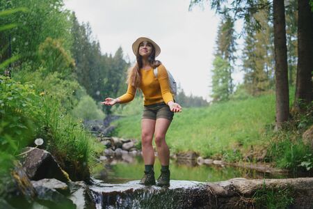 Happy young woman standing by stream on a walk outdoors in summer nature.の写真素材