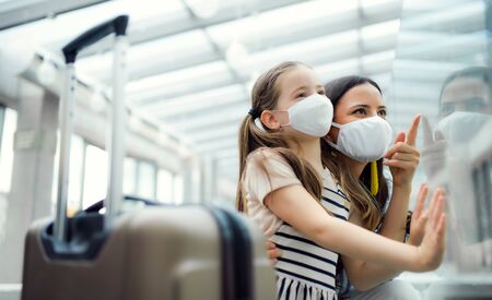 Mother with daughter going on holiday, wearing face masks at the airport.の写真素材