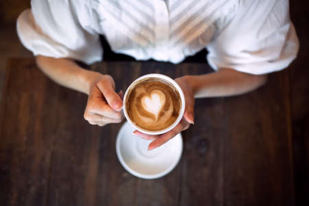 Top view of unrecognizable woman sitting at the table indoors in cafe, holding coffee.の写真素材