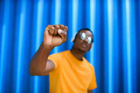 Black man with raised fist standing against blue background, black lives matter concept.
