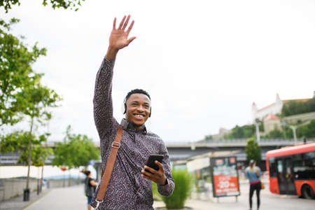 Cheerful young black man commuter outdoors in city, greeting somebody.の写真素材