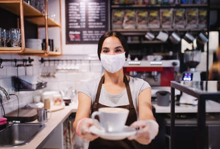 Young woman with face mask working in cafe, serving customers.の写真素材