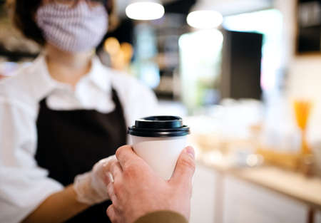 Unrecognizable waitress with face mask working in coffee shop, serving customer.