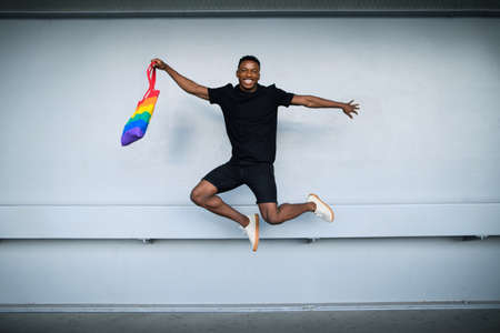 Young black man jumping against white wall background, black lives matter concept.