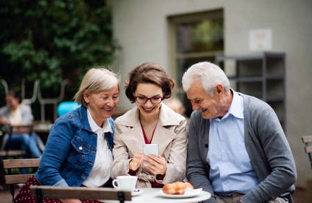 Woman with senior parents sitting outdoors in cafe, using smartphone.
