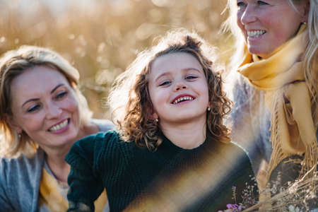 Portrait of small girl with mother and grandmother resting in autumn nature.の写真素材