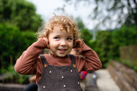 Portrait of small girl standing on farm, holding cherry earrings.