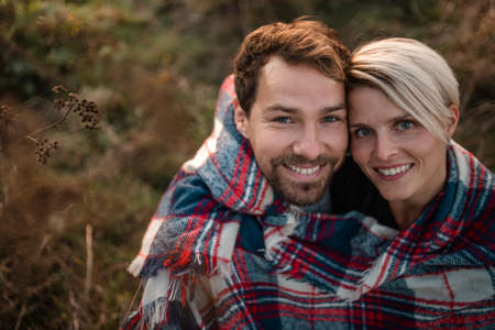 Young couple in love on a walk in autumn nature, looking at camera.
