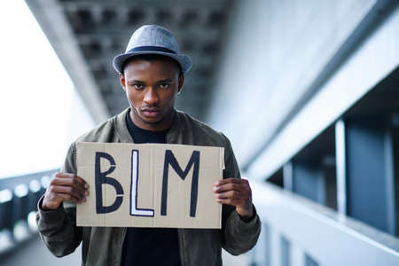 Man with BLM sign standing outdoors, black lives matter concept.