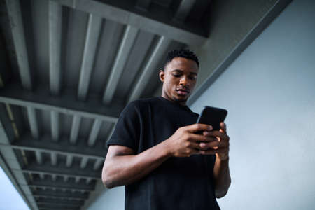 Young black man outdoors in city, using smartphone.の写真素材