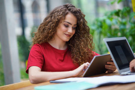 Young woman with tablet sitting indoors in office, working.