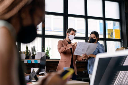 Portrait of young businesspeople with face masks working indoors in office.の写真素材
