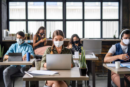Portrait of young businesspeople with face masks working indoors in office.の写真素材