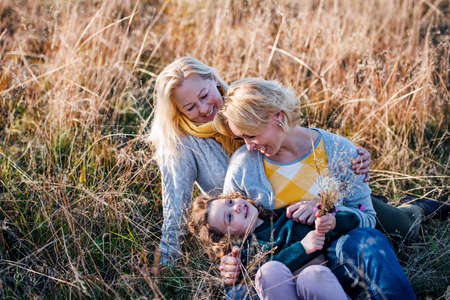 Portrait of small girl with mother and grandmother resting in autumn nature.の写真素材