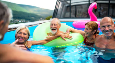 Group of cheerful seniors in swimming pool outdoors in backyard, talking.の写真素材
