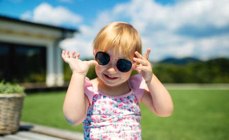 Portrait of small toddler girl with sunglasses outdoors in backyard garden.の写真素材
