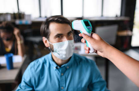 Businessman with face mask working indoors in office, measuring temperature.の写真素材