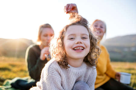 Small girl with mother and grandmother having picnic in nature, having fun.の写真素材