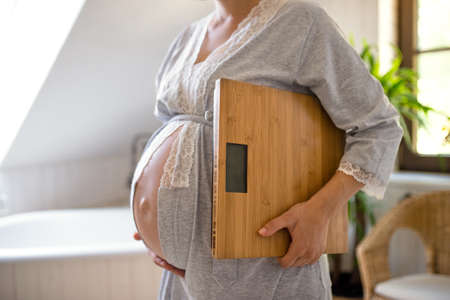 Unrecognizable pregnant woman indoors at home, carrying scales.の写真素材