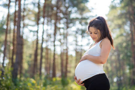 Portrait of happy pregnant woman outdoors in nature, touching her belly.の写真素材