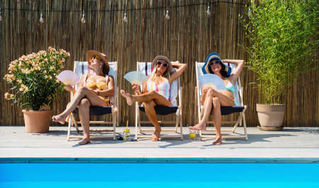 Group of cheerful women seniors sitting by swimming pool outdoors in backyard.の写真素材