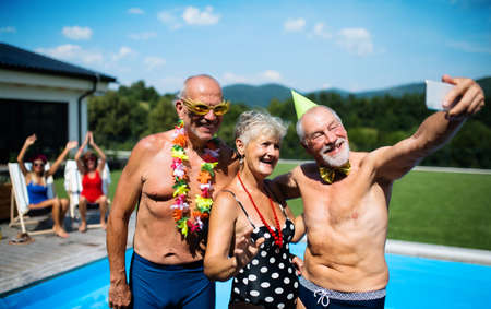 Group of cheerful seniors by swimming pool outdoors in backyard, taking selfie.の写真素材