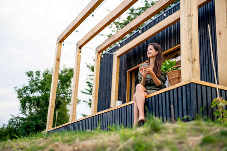 Young woman with smartphone outdoors, weekend away in container house in countryside.