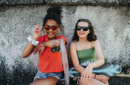 Young teenager girls friends with skateboards outdoors in city, sitting.の写真素材