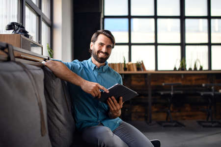 Portrait of young businessman with tablet indoors in office, looking at camera.