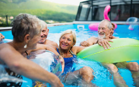 Group of cheerful seniors in swimming pool outdoors in backyard, talking.