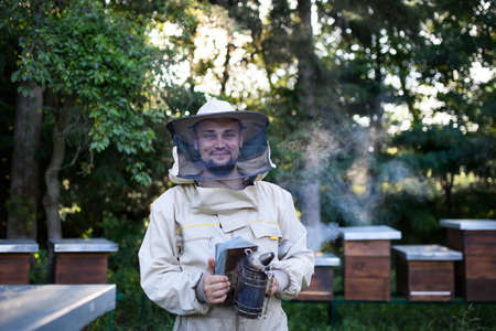 Portrait of man beekeeper working in apiary, holding bee smoker.